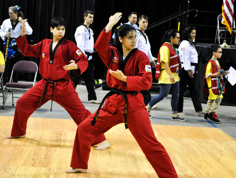 Two students dressed in red taekwondo garb in a taekwondo stance